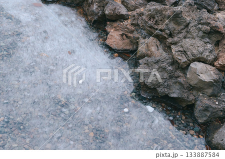 Transparent Ice Surface of a Frozen Lake or Puddle Bordering Rough Basalt Rocks Transparent Ice Surface of a Frozen Lake or Puddle Bordering Rough Basalt Rocks 133887584