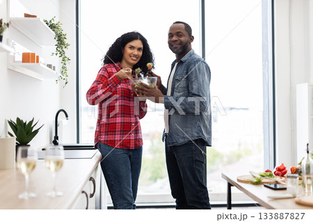 A smiling couple prepares a salad together in a bright, modern kitchen, enjoying a healthy meal. 133887827