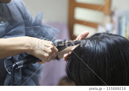 女性の髪にヘアアイロンをかける様子 女性の髪にヘアアイロンをかける様子 133889218