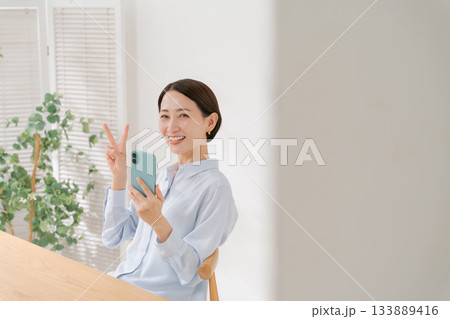 スマホを持ってピースする40代女性 スマホを持ってピースする40代女性 133889416