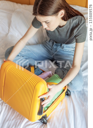 Young woman packing yellow suitcase on hotel bed Young woman packing yellow suitcase on hotel bed 133889576