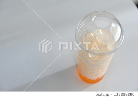 Leftover orange juice with ice in a clear plastic cup. Leftover orange juice with ice in a clear plastic cup. 133889890
