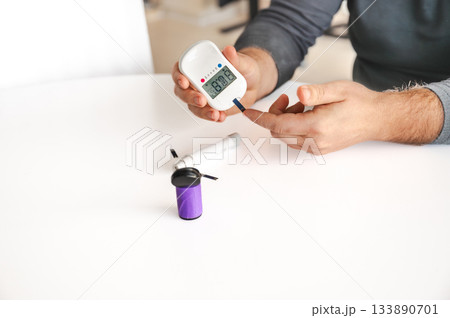 Close-up of a man's hands using a lancet on his finger to test blood glucose level. Concept of diabetes care, glycemia monitoring, and health management. Close-up of a man's hands using a lancet on his finger to test blood glucose level. Concept of diabetes care, glycemia monitoring, and health management. 133890701