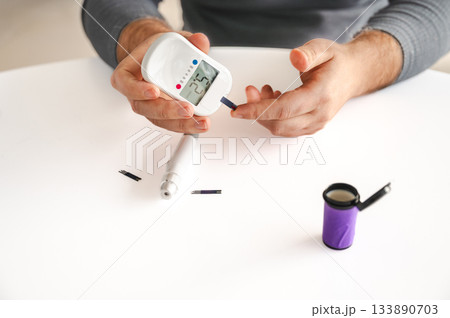 Close-up of a man's hands using a lancet on his finger to test blood glucose level. Concept of diabetes care, glycemia monitoring, and health management. Close-up of a man's hands using a lancet on his finger to test blood glucose level. Concept of diabetes care, glycemia monitoring, and health management. 133890703