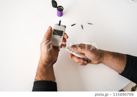 Close-up of a man's hands using a lancet on his finger to test blood glucose level. Concept of diabetes care, glycemia monitoring, and health management. 133890709