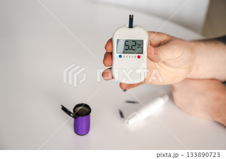 Close-up of a man's hands using a lancet on his finger to test blood glucose level. Concept of diabetes care, glycemia monitoring, and health management. 133890723