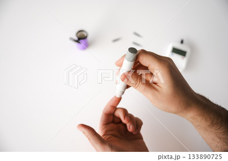 Close-up of a man's hands using a lancet on his finger to test blood glucose level. Concept of diabetes care, glycemia monitoring, and health management. Close-up of a man's hands using a lancet on his finger to test blood glucose level. Concept of diabetes care, glycemia monitoring, and health management. 133890725