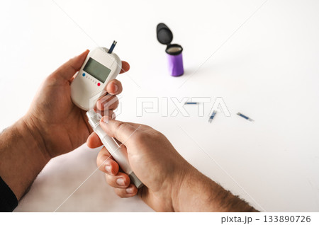 Close-up of a man's hands using a lancet on his finger to test blood glucose level. Concept of diabetes care, glycemia monitoring, and health management. Close-up of a man's hands using a lancet on his finger to test blood glucose level. Concept of diabetes care, glycemia monitoring, and health management. 133890726