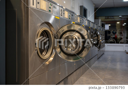 Clean row of modern washing machines in a self-service laundromat. Shared utility space for convenient and efficient laundry. 133890793