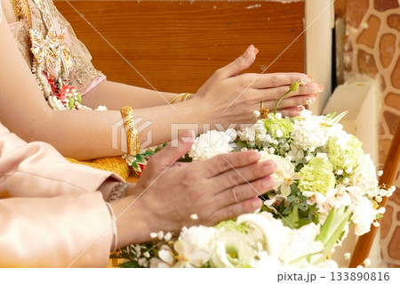 Hands of Thai bride and groom with wedding bouquet at ceremony 133890816
