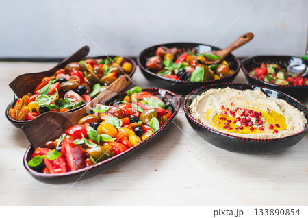 Fresh and colorful vegetarian meal with hummus, mixed green salad, tomatoes, cucumbers, and other vegetables beautifully arranged on a white background. Clean, minimalistic, and healthy food concept. 133890854