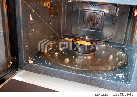 Close-up of a microwave interior with traces of an exploded egg - pieces of shell and egg splattered inside, showing a kitchen accident or cooking fail. 133890946