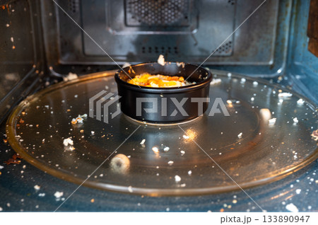 Close-up of a microwave interior with traces of an exploded egg - pieces of shell and egg splattered inside, showing a kitchen accident or cooking fail. 133890947