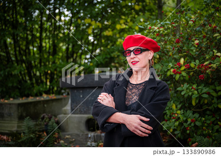 Elegant, well-groomed woman with fashionable style walking in an autumn park on a cloudy day. She wears a red beret, red lipstick, and matching red tights, looking confident and sophisticated. Elegant, well-groomed woman with fashionable style walking in an autumn park on a cloudy day. She wears a red beret, red lipstick, and matching red tights, looking confident and sophisticated. 133890986