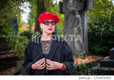 Elegant, well-groomed woman with fashionable style walking in an autumn park on a cloudy day. She wears a red beret, red lipstick, and matching red tights, looking confident and sophisticated. 133891001