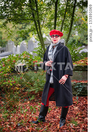 Elegant, well-groomed woman with fashionable style walking in an autumn park on a cloudy day. She wears a red beret, red lipstick, and matching red tights, looking confident and sophisticated. Elegant, well-groomed woman with fashionable style walking in an autumn park on a cloudy day. She wears a red beret, red lipstick, and matching red tights, looking confident and sophisticated. 133891069