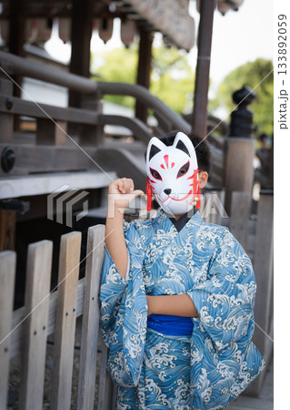 神社の境内で狐の面をつけた浴衣の少年。京都府, 日本 133892059