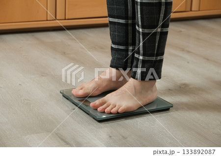 Man weighing himself on modern weighing scales at home, close-up of bare feet. 133892087