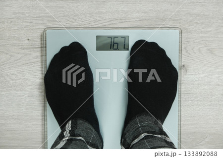 Top View of Feet in Black Socks Standing on Digital Bathroom Scales, Showing Weight 76.7 KG. Top View of Feet in Black Socks Standing on Digital Bathroom Scales, Showing Weight 76.7 KG. 133892088