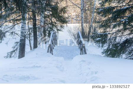 Winter forest scenery with sun shining trough trees. Wooden little bridge. Evening winter forest. High quality photo 133892527