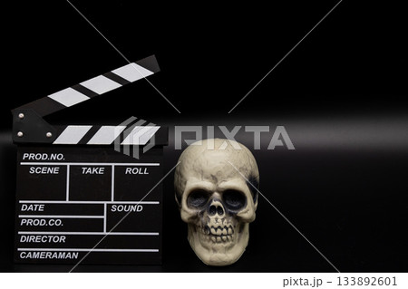 黒背景のカチンコと髑髏、ホラー映画・サスペンス・ミステリーをイメージした素材 133892601