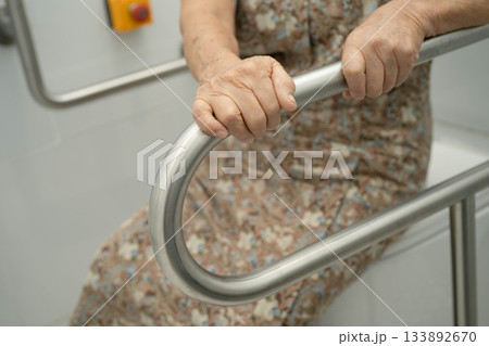 Asian elderly woman patient use toilet support rail in bathroom. 133892670