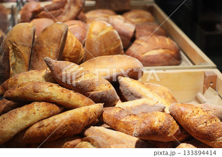 A pile of various fresh loaves of bread in a bakery display. Rustic assortment, golden crusts, artisanal look. 133894414
