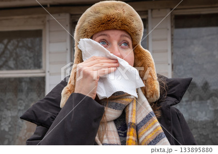 A Caucasian woman in winter clothes wipes her snot outside. Runny nose, bleeding, virus, illness, bloody snot. punch in the face, beatings, domestic violence 133895880