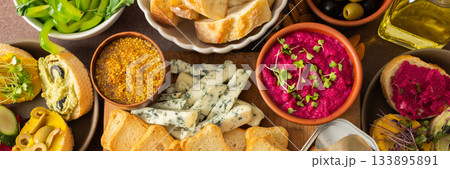 A vibrant charcuterie board showcases a variety of cheese, sausages, hummus, nuts, and sandwiches. Friends gather at a sunny outdoor picnic, enjoying delicious food together, banner 133895891