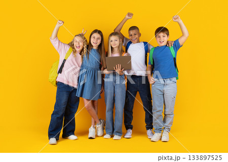 Joyful group of children celebrating while holding laptop in bright studio background 133897525