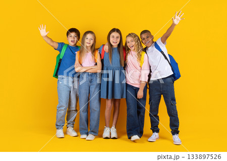 Cheerful group of preteen pupils posing with raised hands on yellow background Cheerful group of preteen pupils posing with raised hands on yellow background 133897526