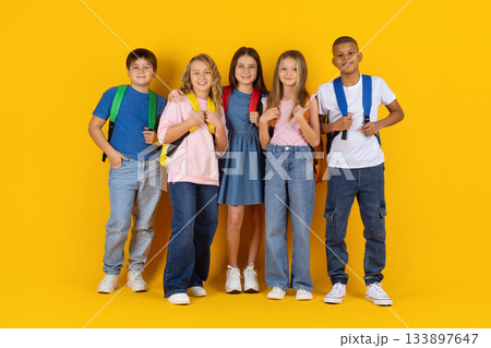 Smiling children with backpacks posing on yellow studio background 133897647