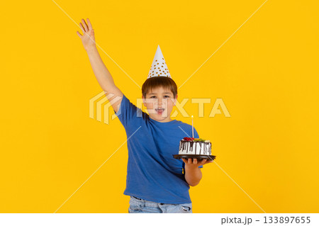 Preteen boy celebrating with birthday cake on bright yellow studio background 133897655