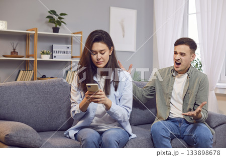 Quarreling young angry man shouting on his wife using mobile phone writing a message Quarreling young angry man shouting on his wife using mobile phone writing a message 133898678
