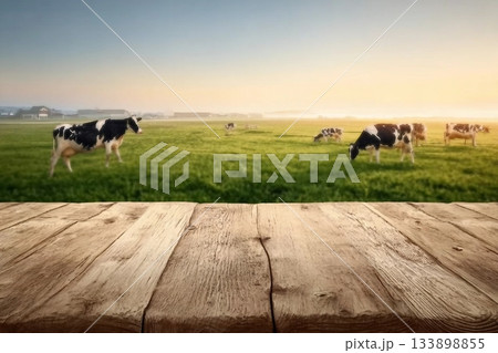 Empty wooden table top with cows in meadow and sunrise background. 133898855