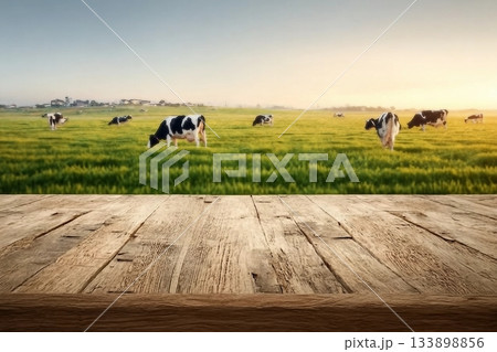 Empty wooden table top with cows in meadow and sunrise background. 133898856