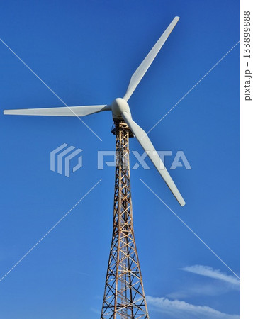 Vertical shot of a wind turbine. A tall, open lattice tower supports a three-bladed rotor 133899888