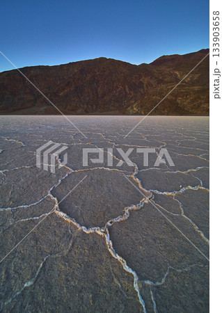 Cracked Salt Flats and Rugged Mountains at Dusk in Badwater Basin Death Valley 133903658