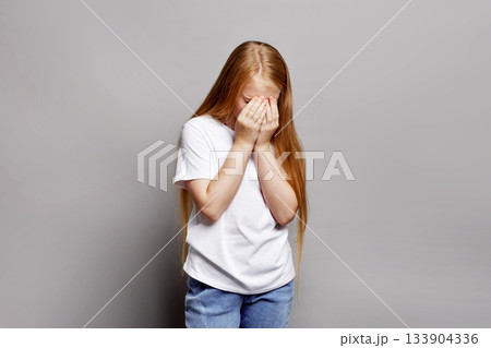 Young girl in studio covering face with hands, looking upset and vulnerable isolated on gray background. Expressive portrait stressed child, teenage emotional struggles and adolescent difficulties Young girl in studio covering face with hands, looking upset and vulnerable isolated on gray background. Expressive portrait stressed child, teenage emotional struggles and adolescent difficulties 133904336