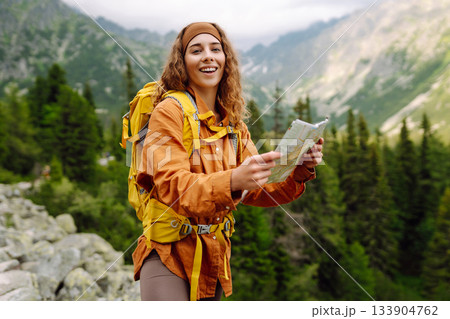 The adventure begins! Beautiful woman traveler with a yellow backpack, holds a map. Vacation concept 133904762