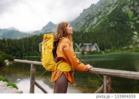Travel Slovakia, Europe. Tourist with a yellow backpack stands against the backdrop of alpine lake. Travel Slovakia, Europe. Tourist with a yellow backpack stands against the backdrop of alpine lake. 133904839