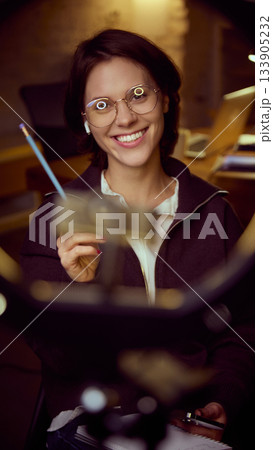 Woman smiling through ring light while explaining material in online session. Woman smiling through ring light while explaining material in online session. 133905232