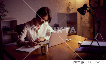 Woman studying at laptop in cozy evening home office Woman studying at laptop in cozy evening home office 133905238