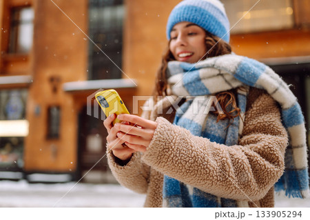 Phone in the hand of young woman in winter street. Online communication. Technology concept. 133905294