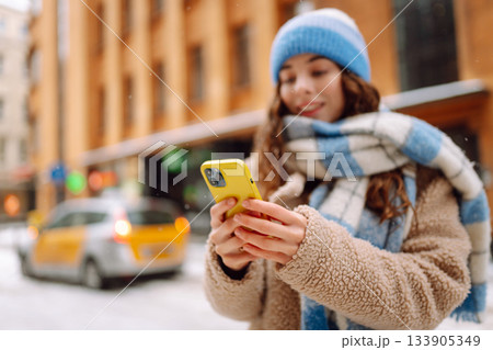 Phone in the hand of young woman in winter street. Online communication. Technology concept. Phone in the hand of young woman in winter street. Online communication. Technology concept. 133905349