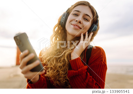 Relaxed woman enjoying music by the waterfront while wearing headphone. Travel and blogging concept Relaxed woman enjoying music by the waterfront while wearing headphone. Travel and blogging concept 133905541
