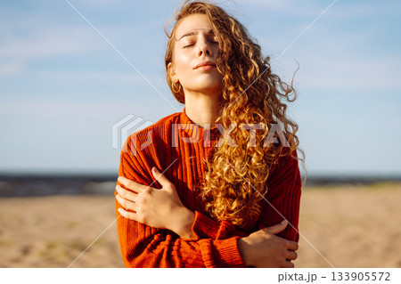 Portrait of a beautiful woman on the beach at sunset at the windy autumn day. Fashion style. Travel Portrait of a beautiful woman on the beach at sunset at the windy autumn day. Fashion style. Travel 133905572