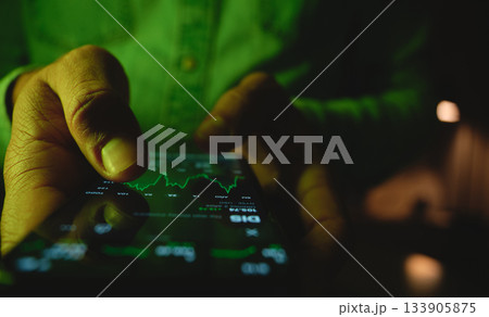 Person checking stock market data on smartphone at night Person checking stock market data on smartphone at night 133905875