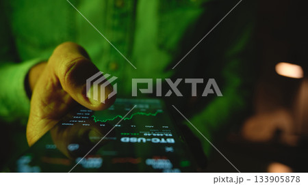 Person checking stock market data on smartphone at night Person checking stock market data on smartphone at night 133905878