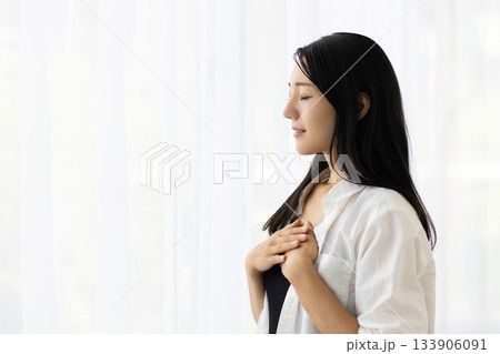 窓辺で胸に手を当て微笑む女性 窓辺で胸に手を当て微笑む女性 133906091